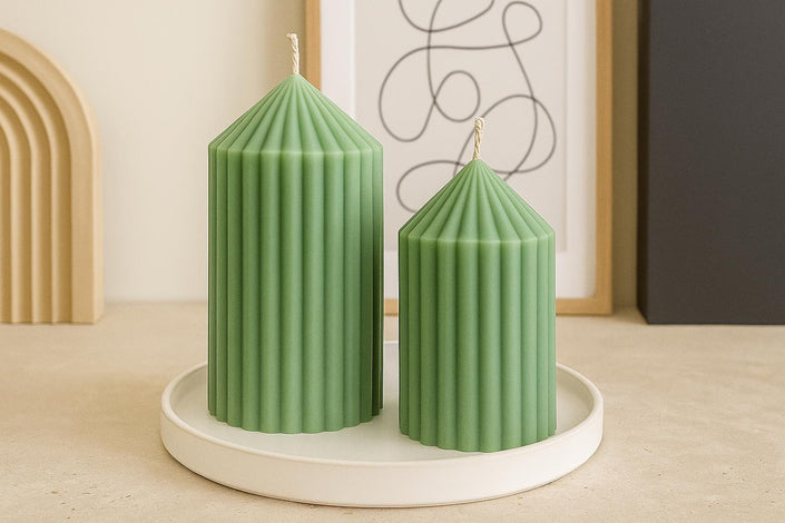 Two green ribbed candles on a white round tray with a minimal background
