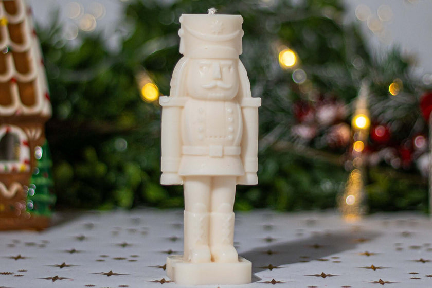 White nutcracker candle standing on a festive table with holiday decor in the background.