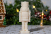 White nutcracker candle standing on a festive table with holiday decor in the background.