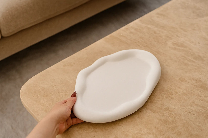 Hand holding a white ceramic dish on a wooden surface with a beige sofa in the background