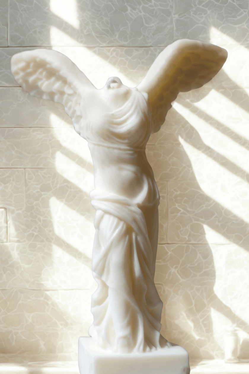 Elegant ivory candle sculpted as the Winged Victory of Samothrace, capturing classical Greek artistry in a refined wax replica.
