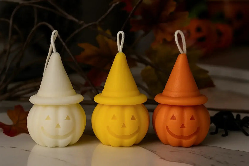 Three Halloween-themed candles in white, yellow, and orange on a reflective surface with a blurred background.