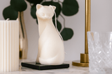 White cat-shaped candle on a marble surface with decorative items in the background