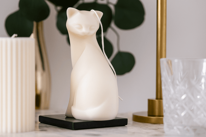 White cat-shaped candle on a marble surface with decorative items in the background