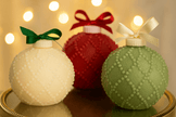 Three decorative ornaments in white, red, and green with ribbons on a reflective surface.