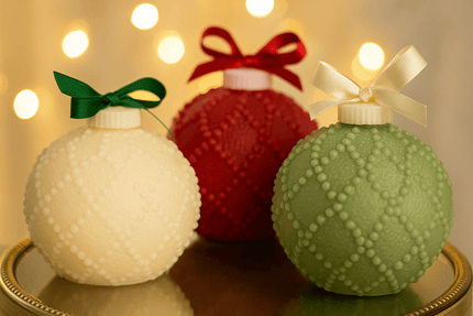 Three decorative ornaments in white, red, and green with ribbons on a reflective surface.