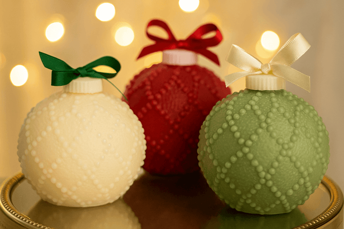Three decorative ornaments in white, red, and green with ribbons on a reflective surface.