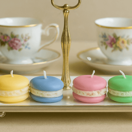 Four colorful macaron-shaped candles on a tray with floral teacups in the background.