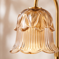 A close-up of a bell-shaped amber glass shade with vertical fluted detailing and a gold metal fixture arm at the top and right edge. Adjustable Height Candle Warmer Lamp — Brass Arch with Fluted Glass Shade