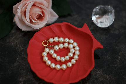 Pearl necklace on a red shell-shaped tray with a pink rose and crystal in the background.