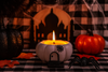 Candle in a pumpkin-shaped holder with pumpkins and spider decorations on a checkered tablecloth.