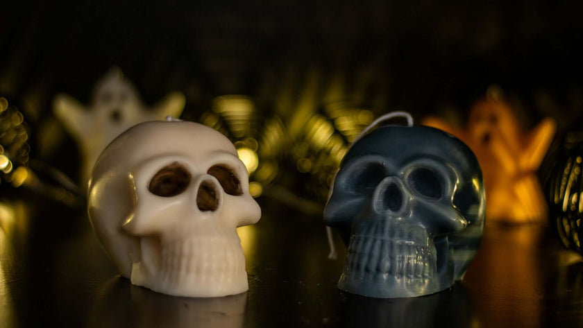 Two gothic skull-shaped candles in white and blue, surrounded by ghost decorations for Halloween ambiance.