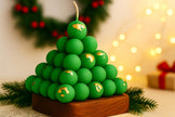Green candle shaped like a Christmas tree with a wooden base, surrounded by festive decorations.
