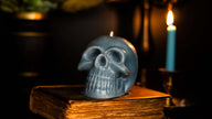 Scented Gothic Skull Candle in natural wax, perfect for Halloween decor, placed on an antique book with candlelight ambiance.