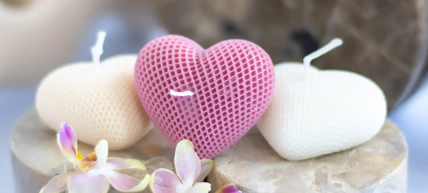 Heart-shaped and round candles on a stone surface with flowers