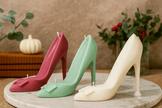 Three high-heeled shoe candles in red, green, and white on a marble surface with a neutral background.