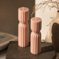 Two pink textured candles on a dark surface with a blurred background