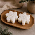 Two snowflake-shaped white candles displayed on a small oval wooden tray, with a neutral fabric background and soft decorative props. Snowflake Candle Gift Set, Handmade Soy Wax Christmas Candles, Winter Decor