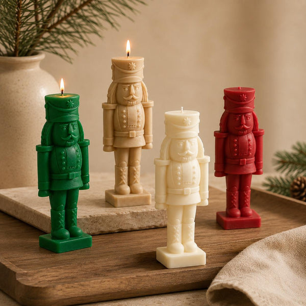 Four nutcracker-shaped candles in green, beige, cream, and red, arranged on a wooden tray with a warm neutral background and holiday greenery.Hand-Poured Nutcracker Candle: Sculptural Soy Wax Christmas Decor