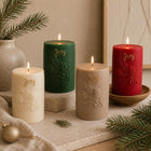 Christmas pillar candle – four lit holiday candles in cream, green, beige and red, embossed with pine branches and 'Joy'