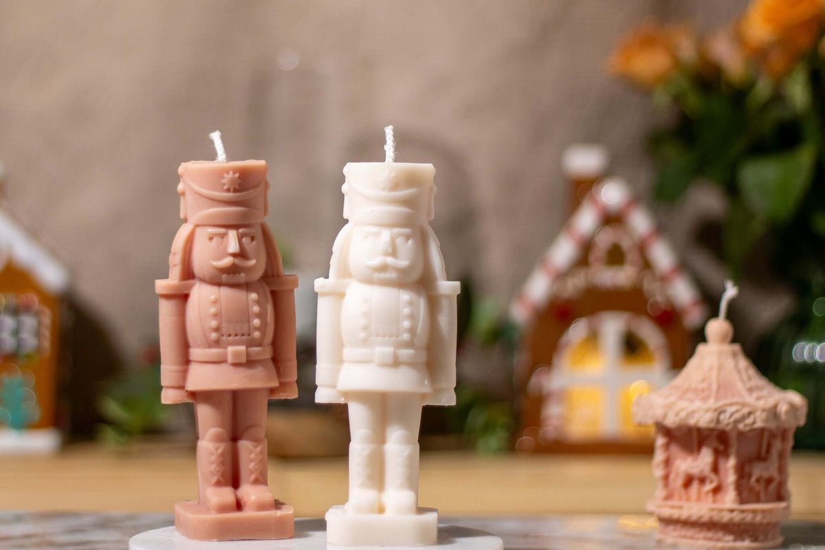 Two nutcracker shaped scented candles in pink and white, surrounded by festive decor for the holiday season.