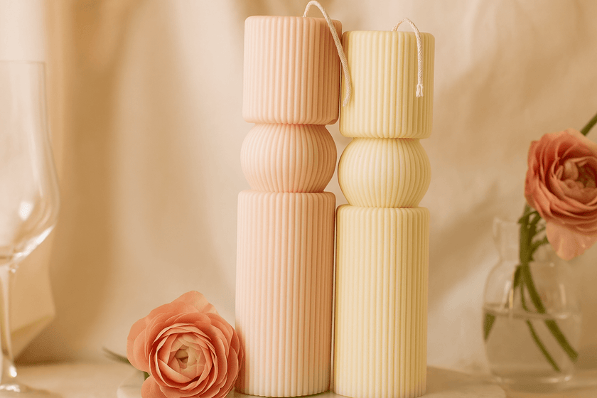 Two cylindrical candles of different heights on a neutral background with flowers.