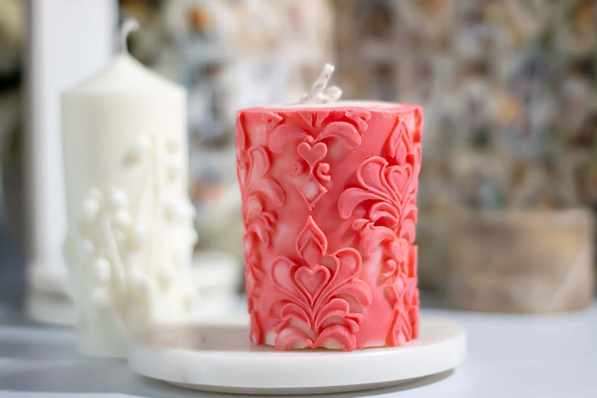 Elegant pink soy wax candle with intricate floral design on a marble tray.