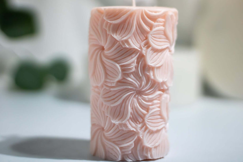 Close-up of the Garden Pillar candle, featuring intricate flower engravings and a soft pastel pink hue.