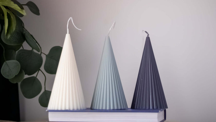 Three handmade cone soy wax candles in white, blue, and dark gray on a book, showcasing their elegant design.