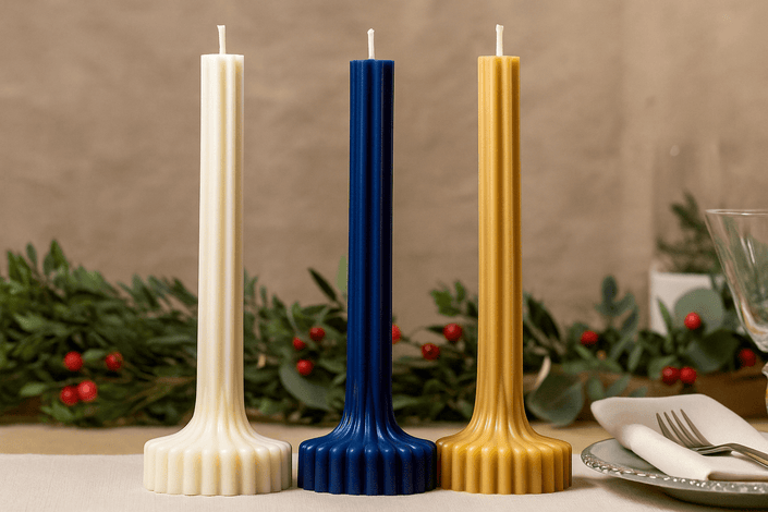 Three tall candles in white, blue, and gold on a table with a decorative background.