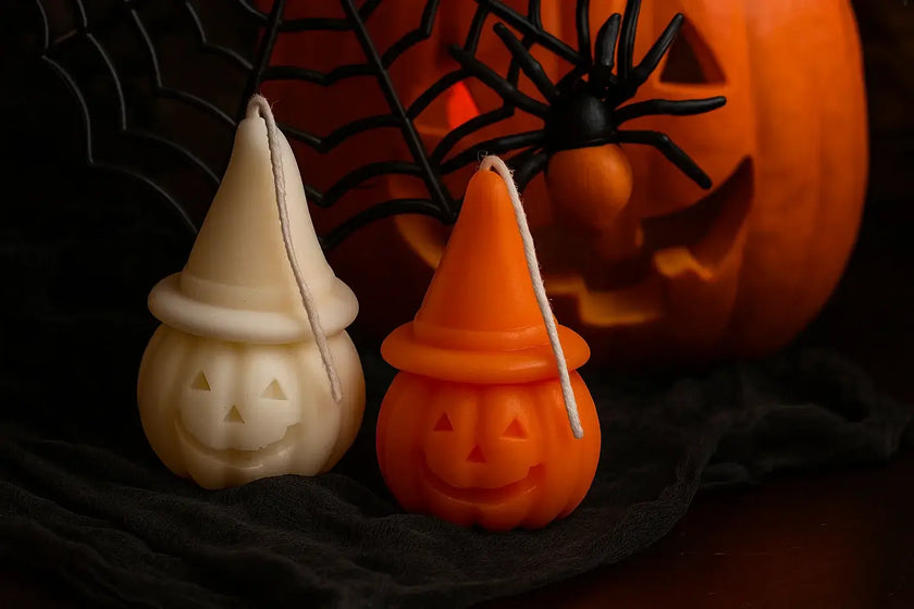 Two Halloween-themed candles shaped like jack-o'-lanterns with a pumpkin and spider web in the background.