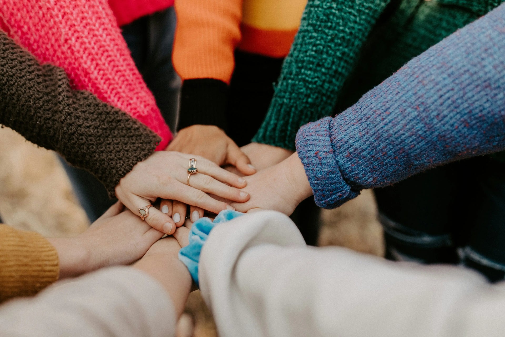 Hands of people stacked together in a circle, wearing colorful clothing.