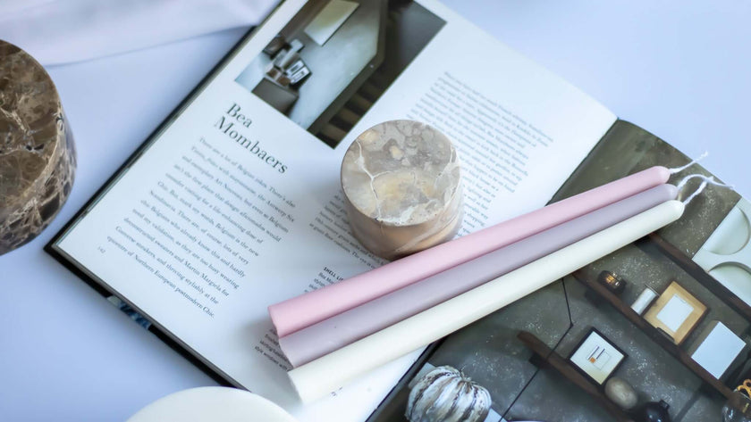 Handmade taper candles in pastel colors beside a coffee table book, showcasing simple elegance for special dinners.
