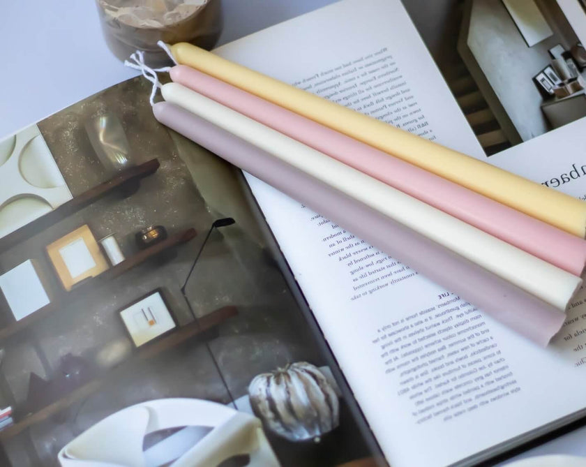 Handmade taper candles in pastel colors on an open magazine, showcasing simple elegance for special dinners.