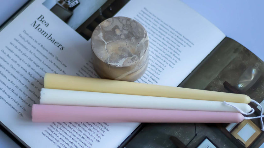 Handmade pastel taper candles in pink, yellow, and white on an open magazine showcasing simple elegance for special dinners.