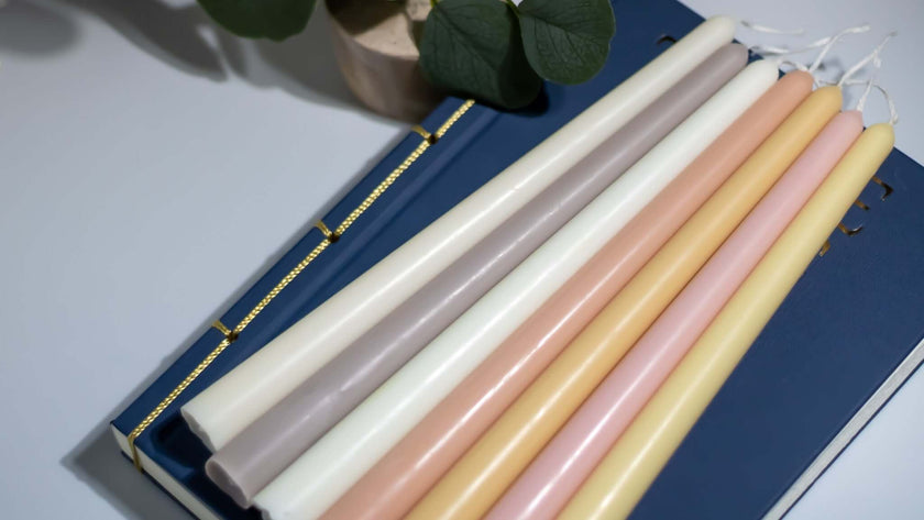 Handmade taper candles in various soft colors arranged on a blue notebook, perfect for elegant dining occasions.